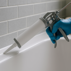 White silicone being tooled along a flexible joint between bathtub and tiled wall in a modern Australian bathroom, highlighting waterproof, mould-resistant flexible silicone – Glues Australia.