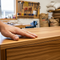 A craftsman's hand is shown in close-up, feeling the perfectly smooth, seamless join of a piece of high-quality wooden furniture. In the background, in a tidy Australian workshop, a box of "Glues Australia - Smooth Finish" is visible.
