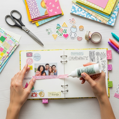A beginner-friendly craft project in progress on a clean white table, featuring hands applying Glues Australia glue to a scrapbook with colorful paper and stickers. Perfect for easy and fun DIY projects for all skill levels