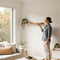 A smiling person in a modern Australian living room proudly displaying a newly installed wooden floating shelf, a simple DIY project achieved with Glues Australia's 'No Primer Needed' collection