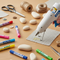 A crafter uses a hot glue gun with EVA hot melt adhesive on a wooden workbench, surrounded by colourful glue sticks and craft supplies. High-quality Hot Glue EVA from Glues Australia for all your crafting and DIY projects