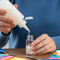 showing a person's hands holding a Glues Australia Refill Pack, actively dispensing glue onto a crafting project